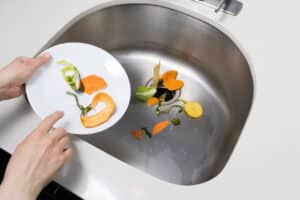 Woman trowing away food scraps in the kitchen sink
